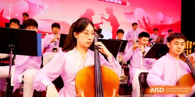 A student musician in a traditional pink ensemble focuses while playing the cello during a concert at Zhengzhou No.4 Middle School.