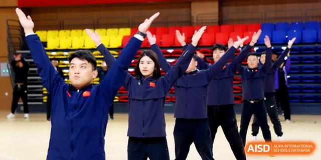 A group of students in blue athletic uniforms perform a synchronized routine with arms raised at Zhengzhou No.4 Middle School.