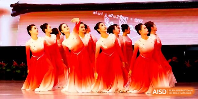 Dancers in elegant red costumes pose together during a choreographed stage performance at Zhengzhou No.4 Middle School.