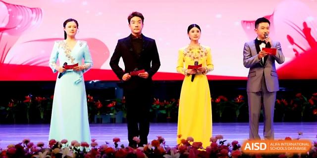 Two formal presenters stand on a stage in elegant attire to host a school ceremony at Zhengzhou No.4 Middle School.
