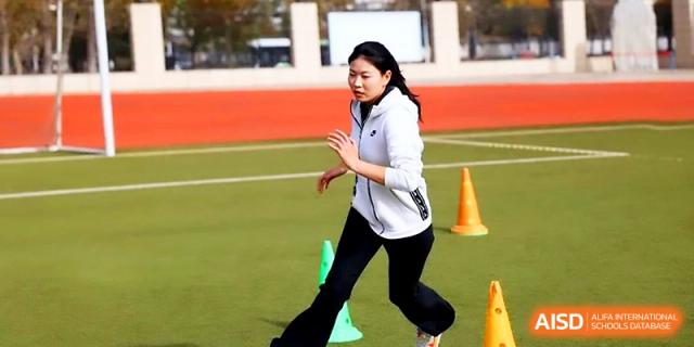 A student in a white jacket and black leggings practices running drills on an outdoor field at Zhengzhou No.4 Middle School.