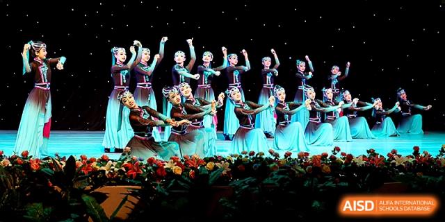 A large dance troupe in blue and white costumes performs a synchronized routine on stage at Zhengzhou No.4 Middle School.