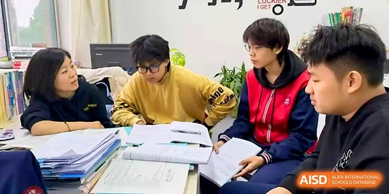 Two students in school uniforms sit at a desk together, deeply focused on reviewing their textbooks at Zibo International Academy At Hi-Tech Zone.