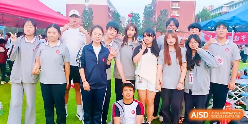 A group of diverse students and staff members pose together for a friendly group photo outdoors at Zibo International Academy At Hi-Tech Zone.