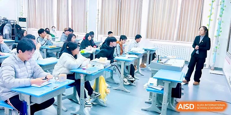 Students in a modern classroom sit at blue desks, listening attentively to a lecture during their studies at Zibo International Academy At Hi-Tech Zone.
