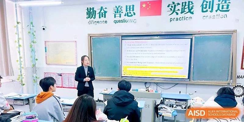 A teacher stands by a chalkboard and a digital monitor to explain a complex lesson to the class at Zibo International Academy At Hi-Tech Zone.