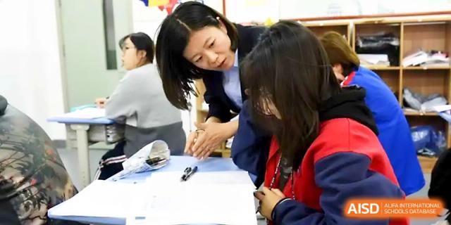 A teacher leans in to help a student with their work during a focused classroom session at Zibo International Academy At Hi-Tech Zone.