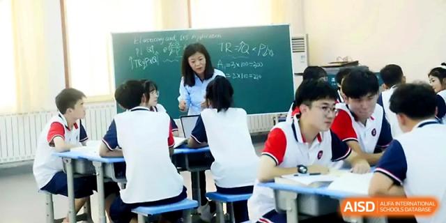 A teacher points to a green chalkboard filled with equations while instructing students in a lab at Zibo International Academy At Hi-Tech Zone.