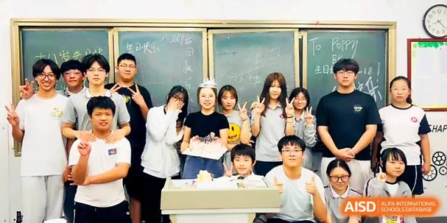 Students and a teacher gather around a desk for a joyful celebration or birthday party inside a classroom at Zibo International Academy At Hi-Tech Zone.