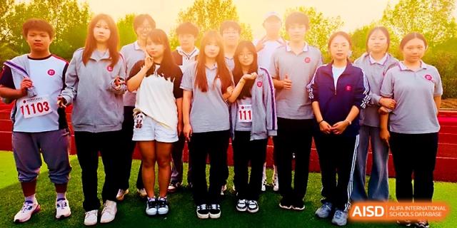 A group of students in grey and white uniforms stand together on a green field during a sunny day at Zibo International Academy At Hi-Tech Zone.