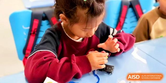 A young girl carefully assembles small electronic parts during a hands-on STEM activity at Zibo International Academy At Hi-Tech Zone.