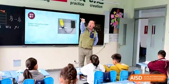 A teacher demonstrates a science experiment using electronic components in front of a classroom at Zibo International Academy At Hi-Tech Zone.