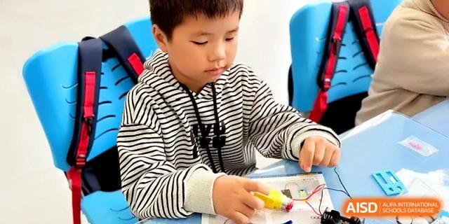 A young boy in a striped shirt works on a robotics project with various electronic components at Zibo International Academy At Hi-Tech Zone.