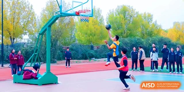 A student athlete jumps for a layup during an outdoor basketball game on the school court at Zibo International Academy At Hi-Tech Zone.