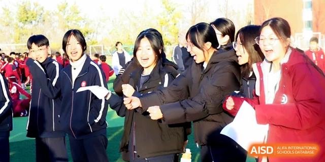 Female students laugh and cheer while participating in a tug-of-war event on the athletic field at Zibo International Academy At Hi-Tech Zone.
