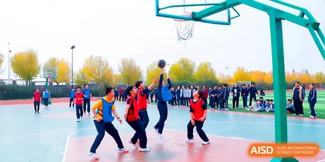 A student in mid-air attempts a layup during a basketball game with classmates watching at Zibo International Academy At Hi-Tech Zone.