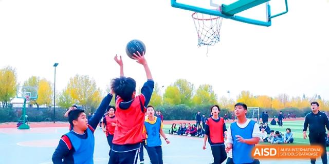 A young student in a red jersey takes a jump shot during a basketball game on the outdoor court at Zibo International Academy At Hi-Tech Zone.