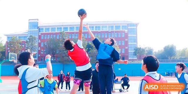 Two students jump high for a tip-off at the start of a basketball match on the school grounds at Zibo International Academy At Hi-Tech Zone.