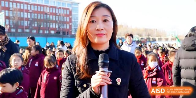 A female staff member speaks into a microphone, leading an assembly for students on the field at Zibo International Academy At Hi-Tech Zone.