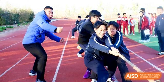 Students in blue uniforms exert effort during a tug-of-war match on the red athletic track at Zibo International Academy At Hi-Tech Zone.