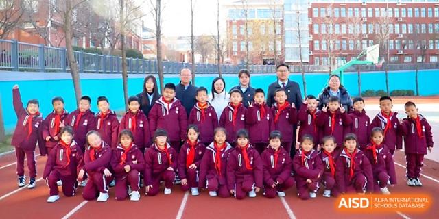 A large group of primary students and teachers pose for a commemorative photo on the track at Zibo International Academy At Hi-Tech Zone.