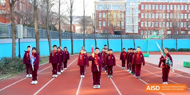 Students in red uniforms stand in neat rows during a formal outdoor school assembly at Zibo International Academy At Hi-Tech Zone.