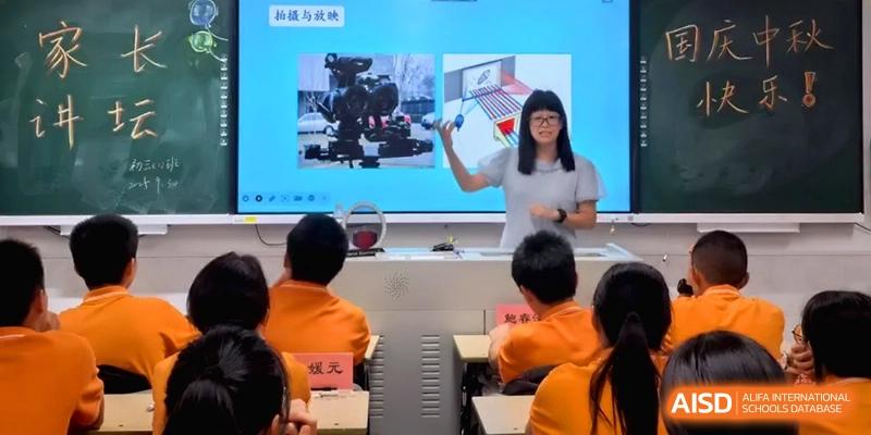 A female teacher gives a presentation on a large digital screen to students in orange uniforms at the Affiliated High School of Fujian Normal University.