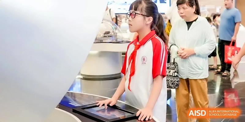 A student in a red and white uniform interacts with a touch-screen display at a science exhibit for the Affiliated High School of Fujian Normal University.