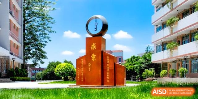 A large orange monument with a silver key ring sculpture on top stands under a clear blue sky at the Affiliated High School of Fujian Normal University.