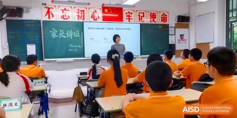 Students in orange shirts sit at desks while a teacher presents a slide in a modern classroom at the Affiliated High School of Fujian Normal University.