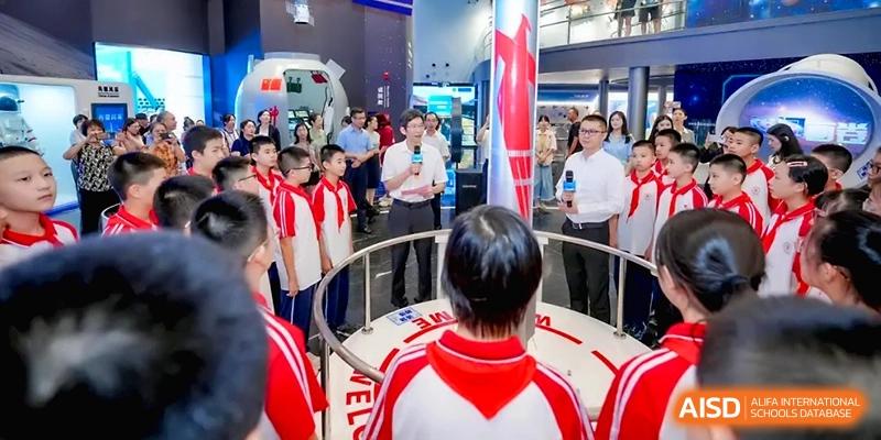 A man with a microphone addresses a group of students standing in a circle around a museum exhibit at the Affiliated High School of Fujian Normal University.