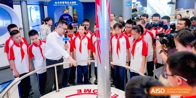 Students in red and white uniforms listen to a guided tour near a rocket display during an outing for the Affiliated High School of Fujian Normal University.
