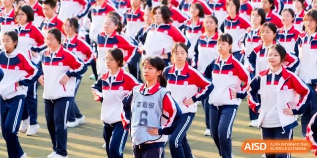 Students in red and blue athletic uniforms stand in formation on a field at the Affiliated High School of Fujian Normal University.