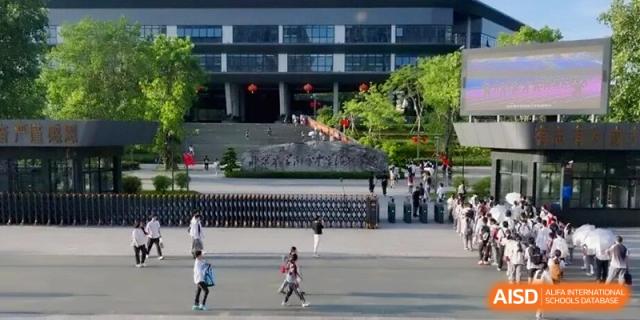 Exterior view of students walking in the plaza and entrance of the modern campus building at the Affiliated High School Of Peking University Haikou.
