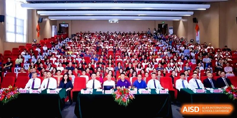A formal stage view of school officials and a large seated student audience during a gala at the Affiliated High School Of Peking University Haikou.