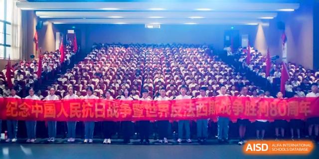 Students holding a long red ceremonial banner during a large indoor gathering or assembly at the Affiliated High School Of Peking University Haikou.