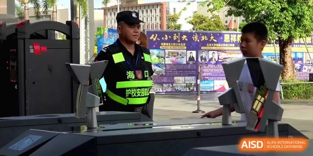 A security officer in a high-visibility vest standing on duty near the campus entrance at the Affiliated High School Of Peking University Haikou.