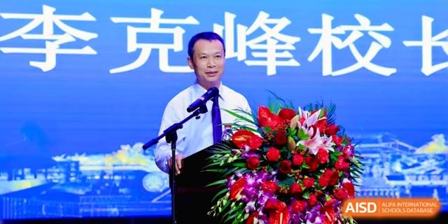 A speaker stands at a podium with floral arrangements during a formal school presentation at the Affiliated High School Of Peking University Haikou.