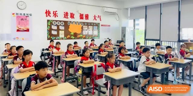 Young elementary students sit at their desks in a colorful and organized classroom at the Affiliated High School Of Peking University Haikou.