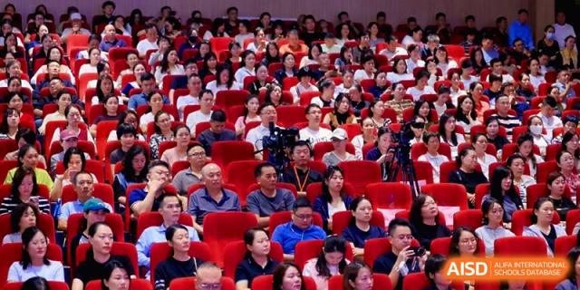 A diverse audience of parents and students sits in red chairs during a school meeting at the Affiliated High School Of Peking University Haikou.