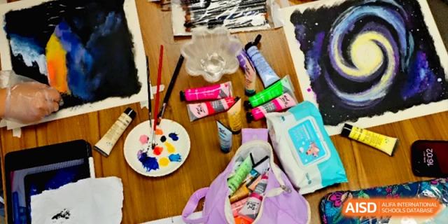 Various art supplies including paint tubes and palettes are spread out on a desk at the Affiliated High School Of Peking University Haikou.