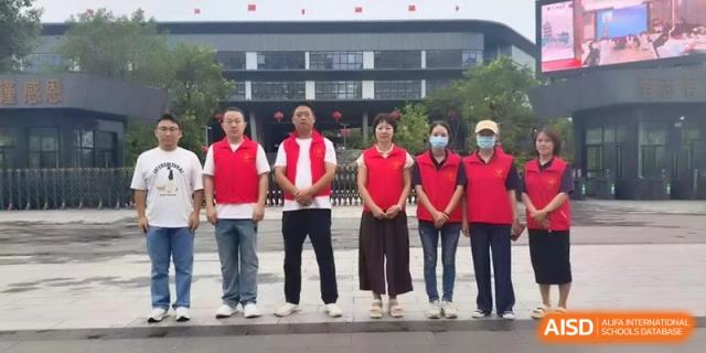 Staff members in red vests stand together for a group photo outside the main building at the Affiliated High School Of Peking University Haikou.