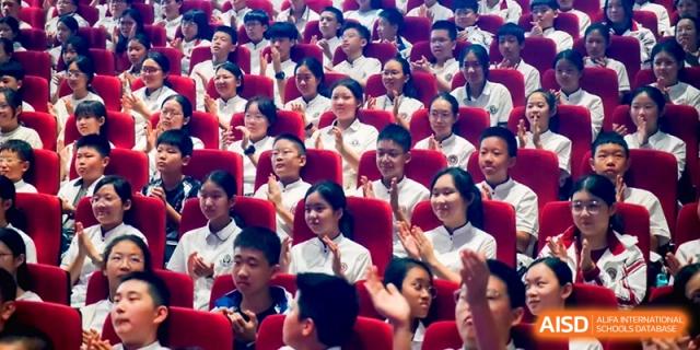 Students seated in a theater setting raise their hands to answer a question during a talk at the Affiliated High School Of Peking University Haikou.