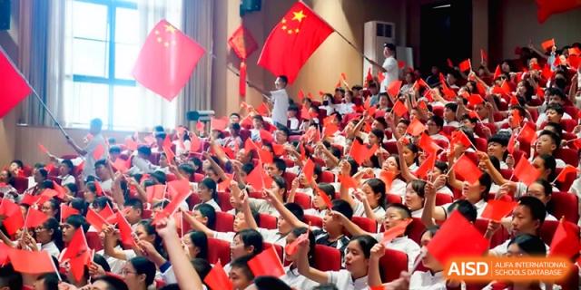 Students wave small flags and cheer during a high-energy school spirit assembly at the Affiliated High School Of Peking University Haikou.