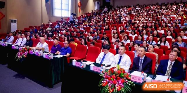 School leaders sit at a front table decorated with flowers during a formal conference at the Affiliated High School Of Peking University Haikou.