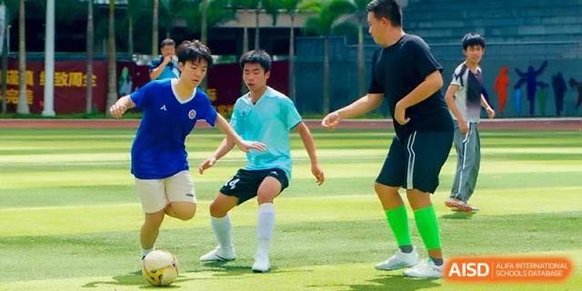 Students in blue jerseys competing in a soccer match on the campus grass field at the Affiliated High School Of Peking University Haikou.