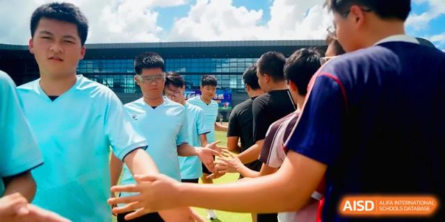 Soccer players in blue uniforms shaking hands after a game on the field at the Affiliated High School Of Peking University Haikou.