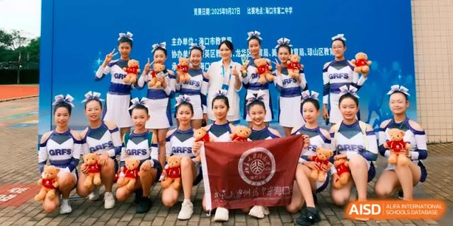 Students holding a maroon school flag and trophies after a competition at the Affiliated High School Of Peking University Haikou.
