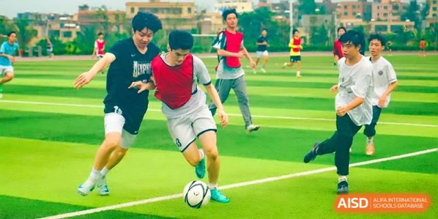 A student athlete in a red vest dribbling a soccer ball during practice at the Affiliated High School Of Peking University Haikou.
