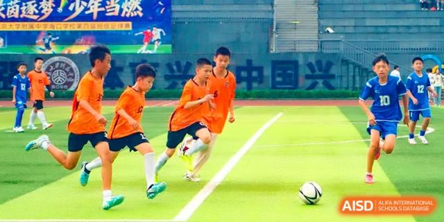 Young students in orange jerseys playing soccer on the professional turf at the Affiliated High School Of Peking University Haikou.